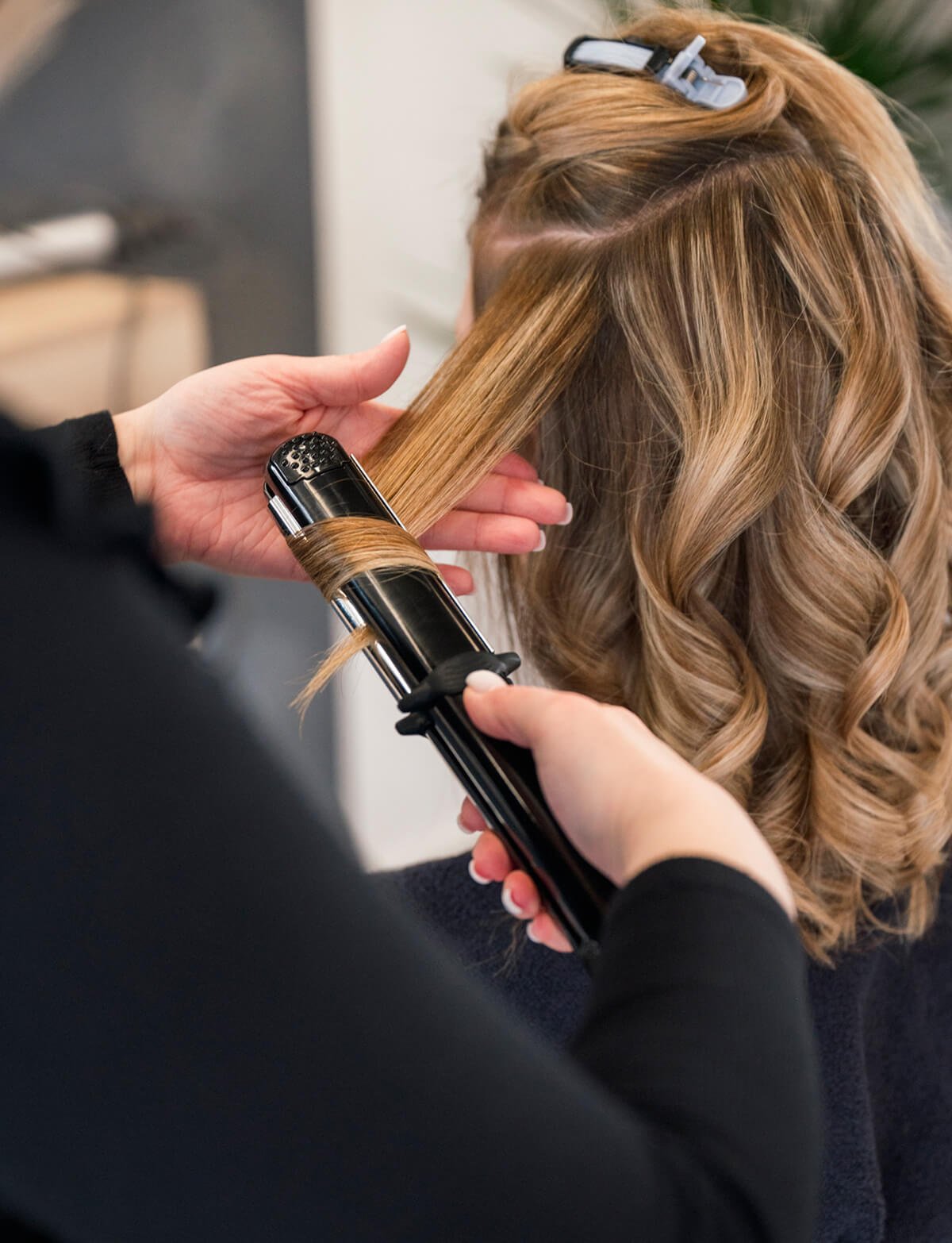 Professional stylist using a curling iron for hair styling and creating beautiful waves for a client at Artysto Salon.
