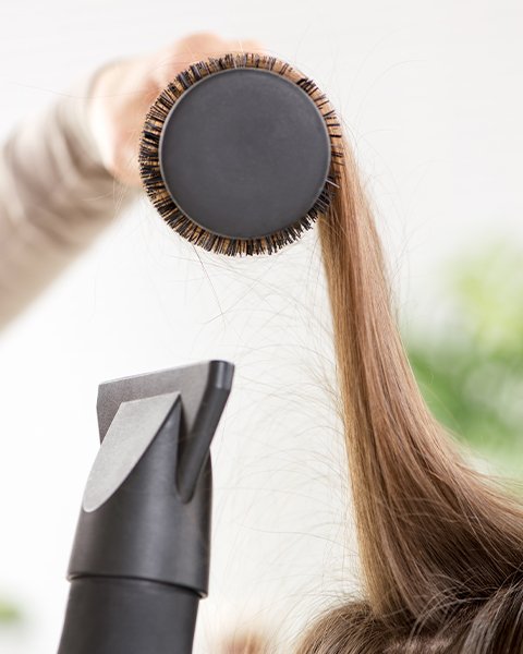 Professional stylist performing a Blast Dry service with a round brush to achieve silky, soft, and revitalized hair.