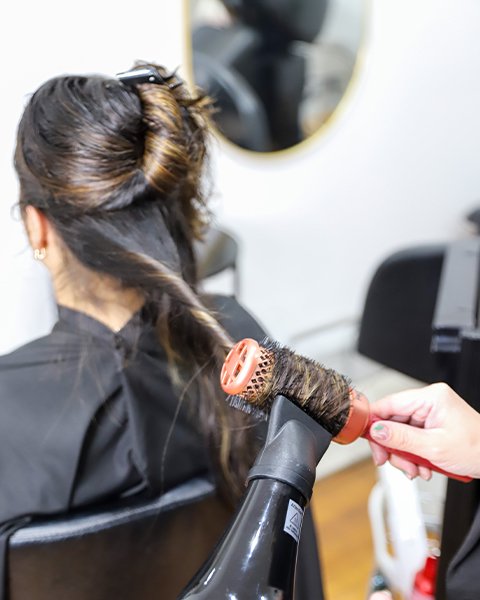 Professional Artysto stylist performing a blow dry and styling service using a round brush for smooth, sleek, and outward curls.