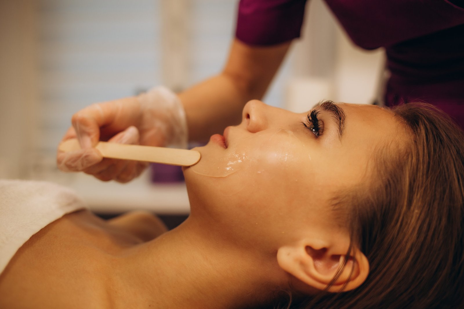 Professional cosmetologist applying a soothing facial mask to a client's face during a deep skin treatment for rejuvenation and a healthy glow.