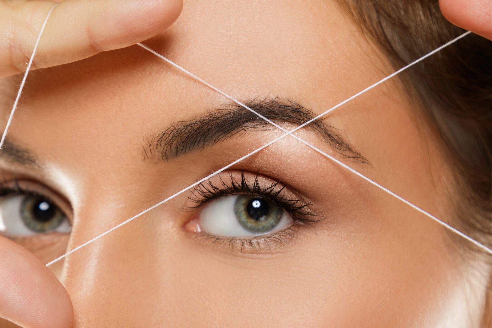 technician defining a woman's eyebrows using threading for a precise, clean, and polished look.