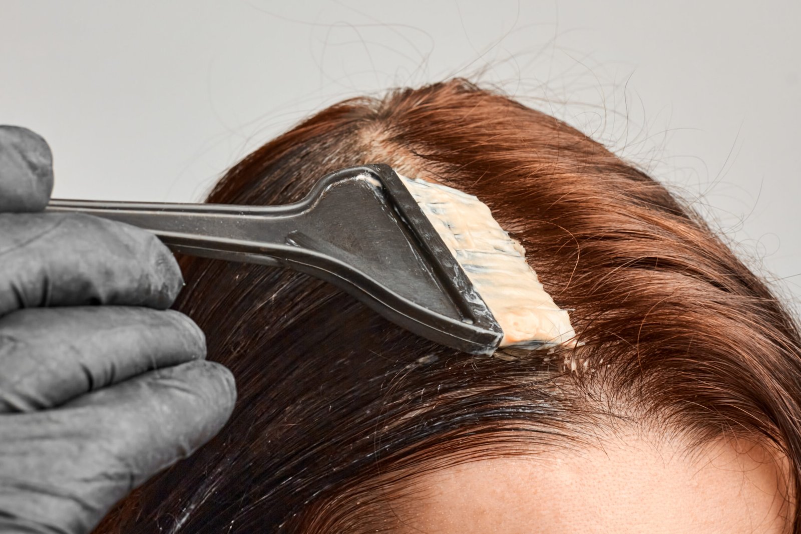 Closeup of a skilled Artysto colorist applying hair color to the roots with a brush for a seamless Root Touch-Up service.